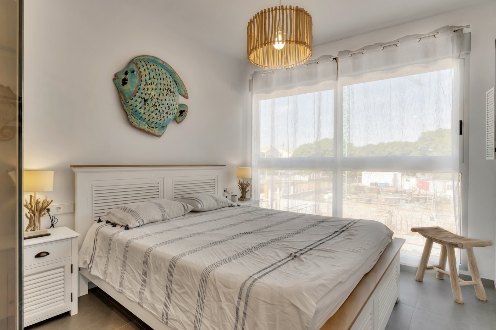 Bright bedroom featuring a white wooden bed frame, marine-themed decor, a bamboo pendant light, and a large window for natural light.