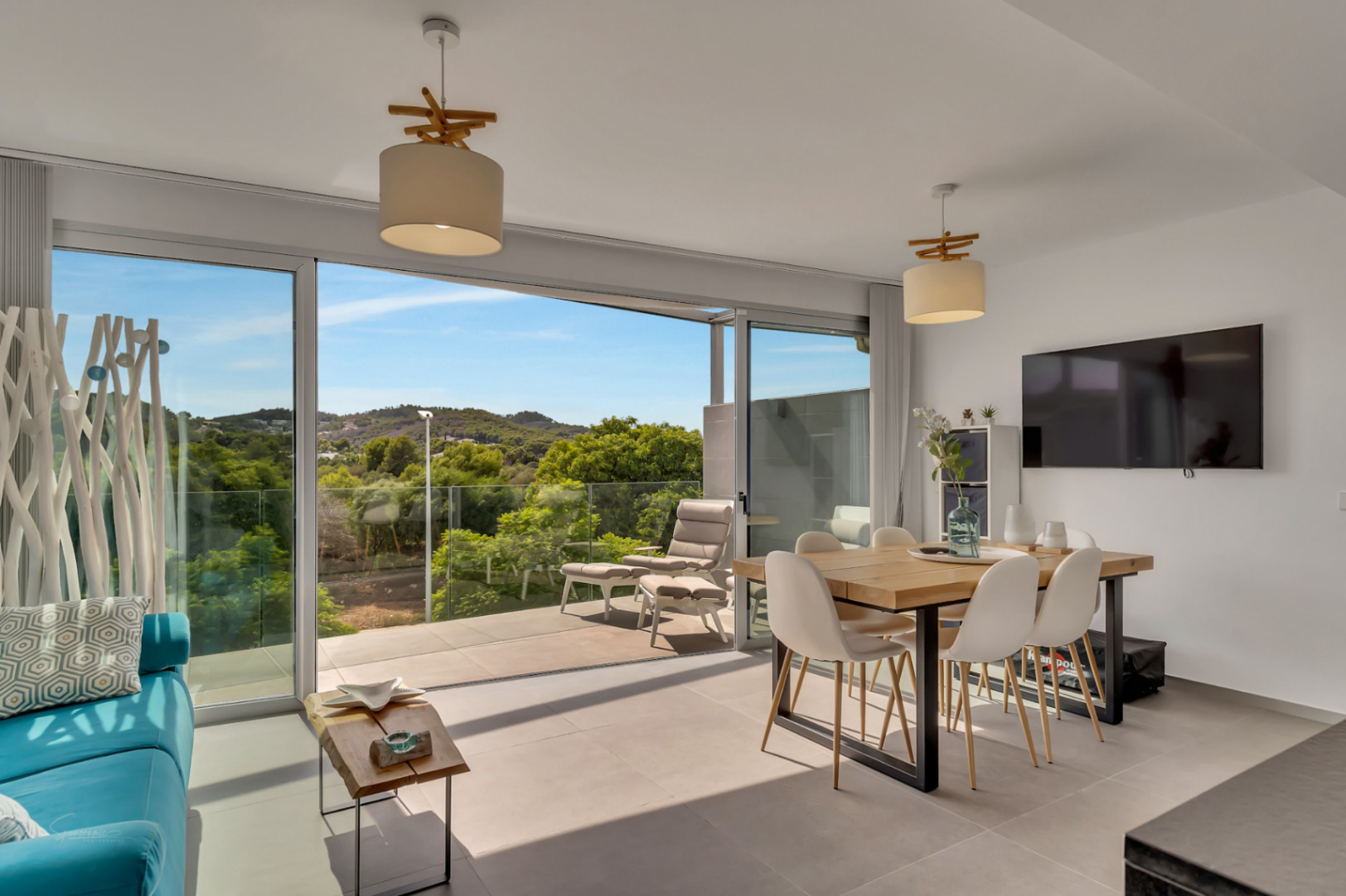 Bright living and dining area featuring floor-to-ceiling sliding glass doors that open to a balcony with expansive views of the surrounding greenery and hills.