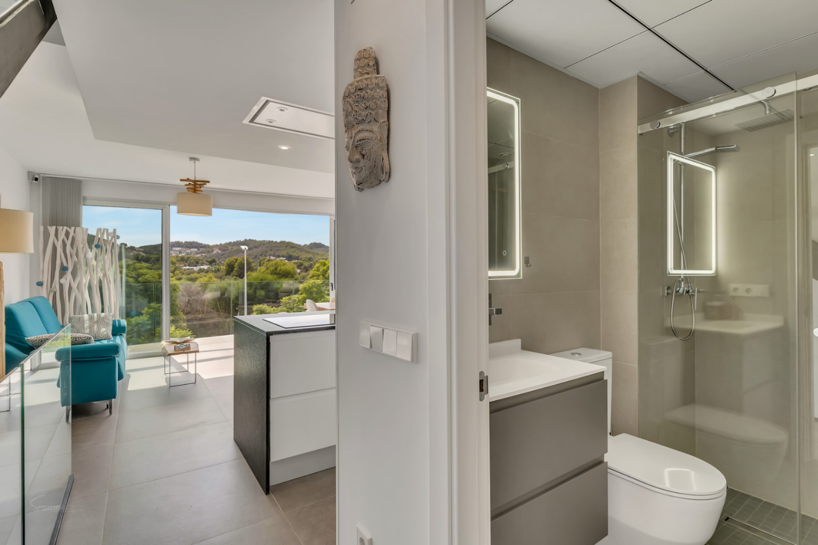 Hallway view featuring a modern bathroom with a backlit mirror and glass shower, alongside an open-plan living space with large windows and landscape views.