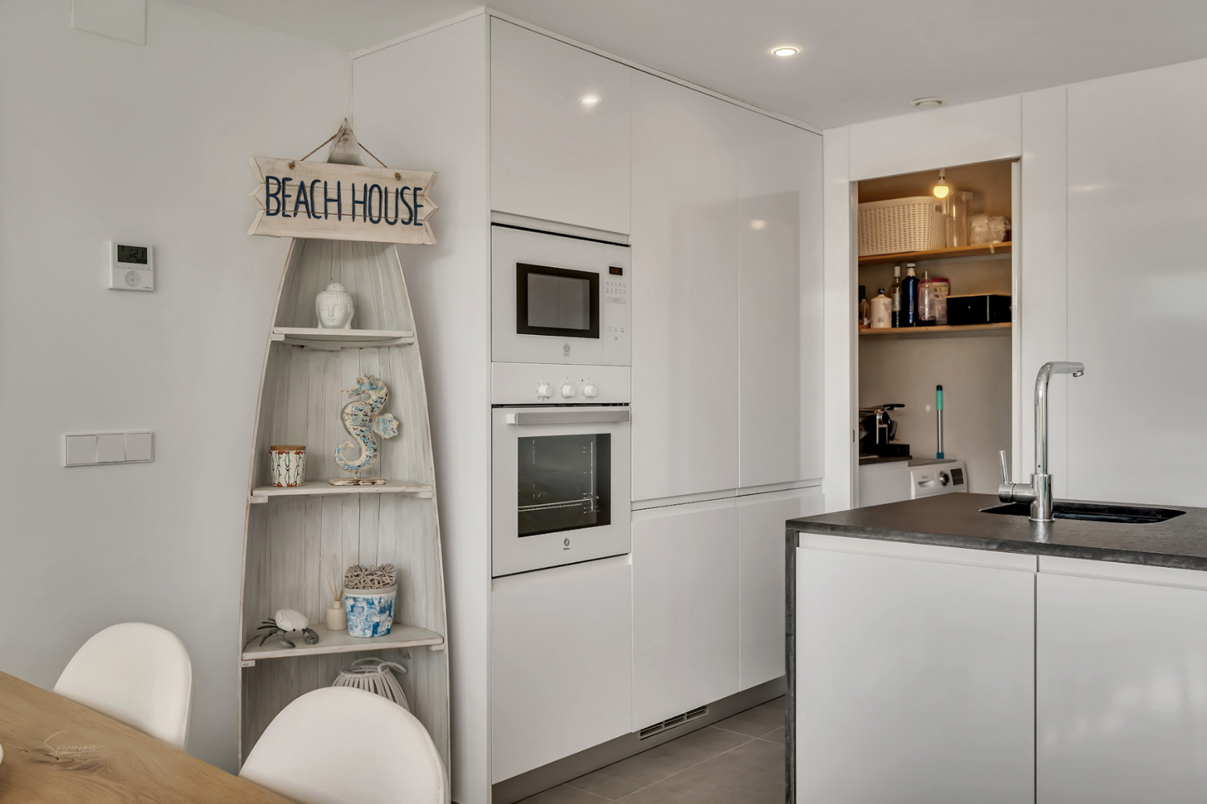 Modern kitchen featuring high-gloss white cabinetry, integrated appliances, and an adjacent laundry area with nautical-themed shelving.
