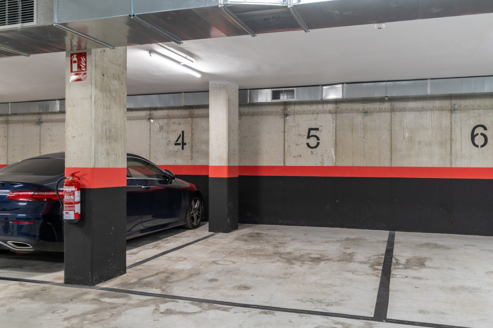 Numbered underground parking space in a modern building, featuring exposed concrete walls, ventilation ducts, and integrated fire safety systems.
