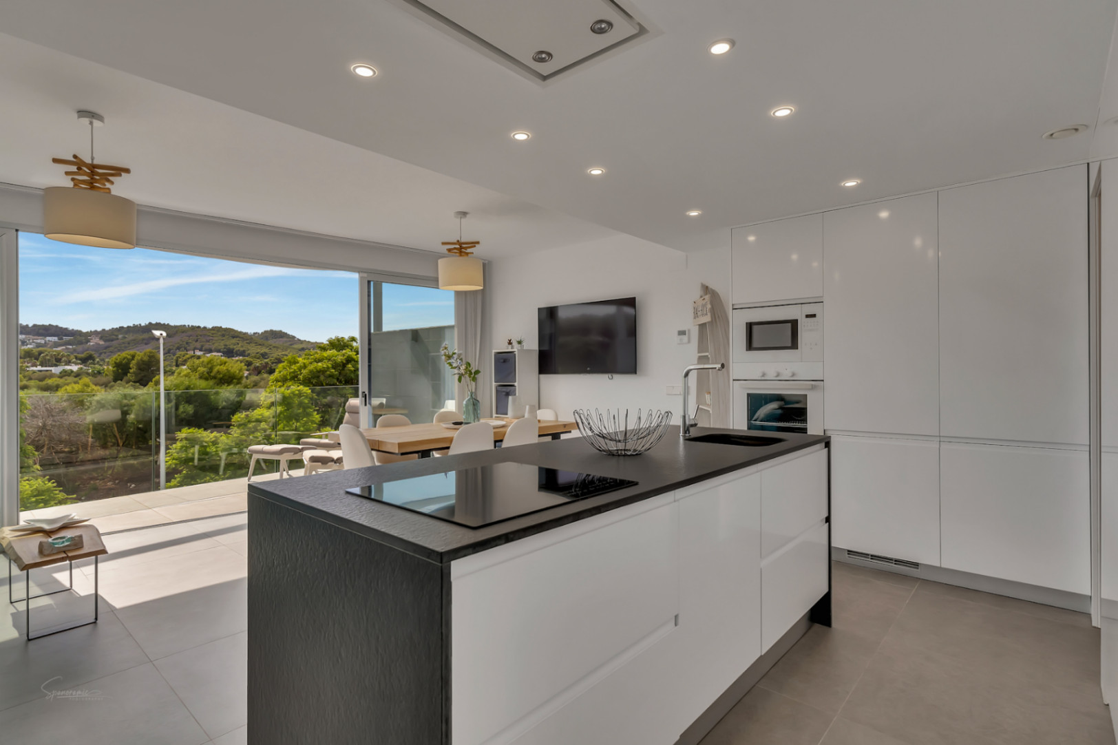 Open-plan kitchen featuring a large island with a dark textured countertop, integrated appliances, and seamless access to a terrace overlooking green landscapes.