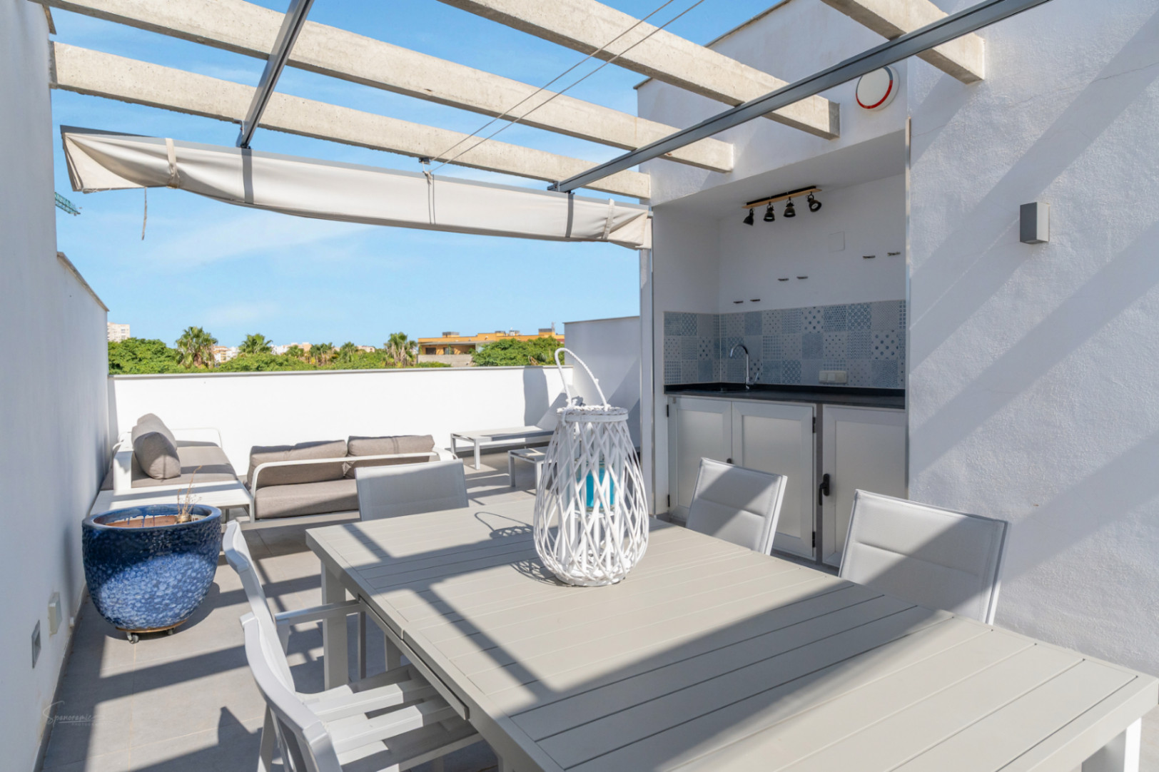 Private rooftop terrace featuring a summer kitchen with tiled backsplash, outdoor dining area, and lounge seating under a concrete pergola with retractable awning.