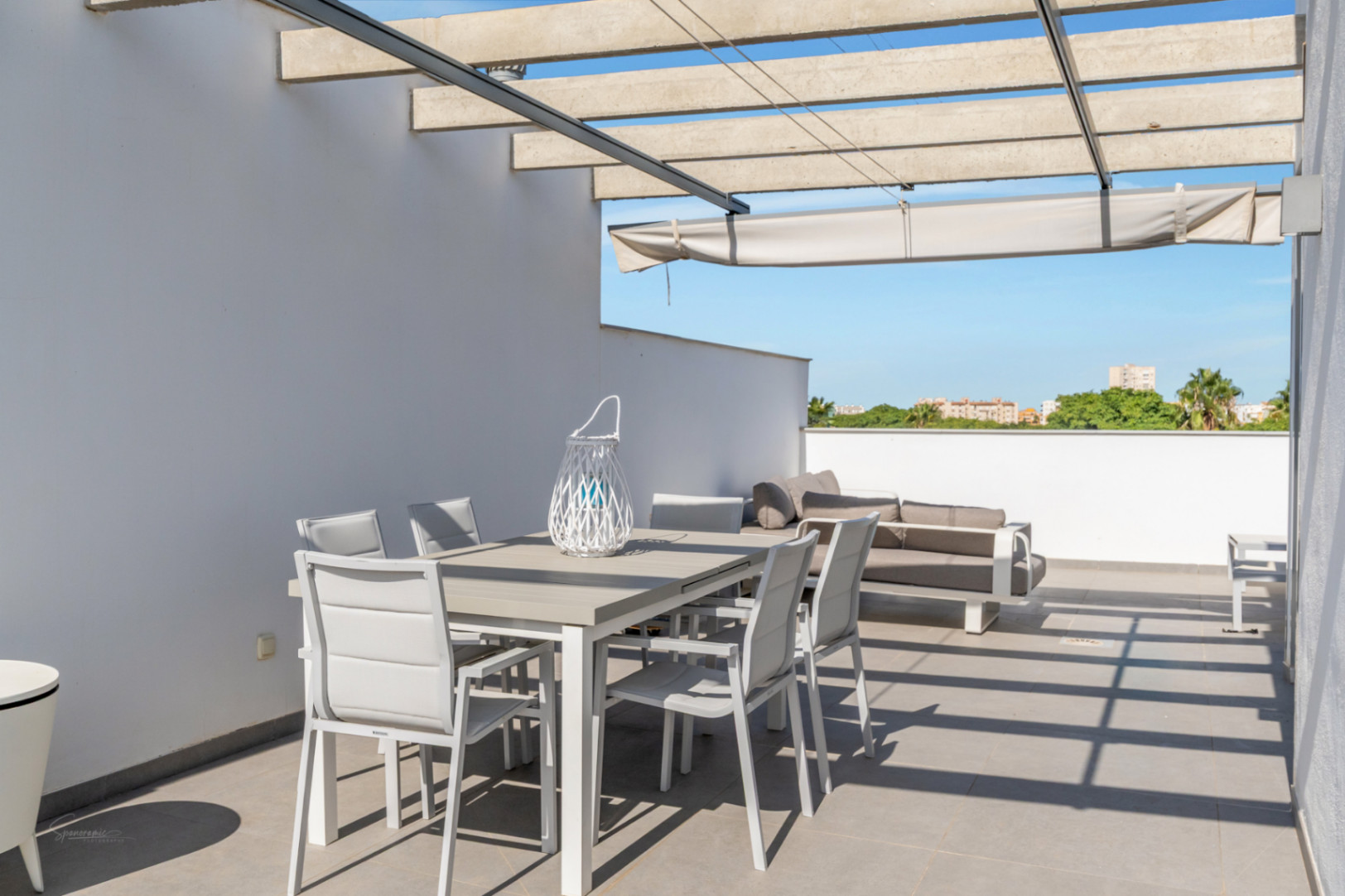 Private rooftop terrace featuring an outdoor dining set, lounge sofa, and concrete pergola with a retractable awning over grey tiled flooring.