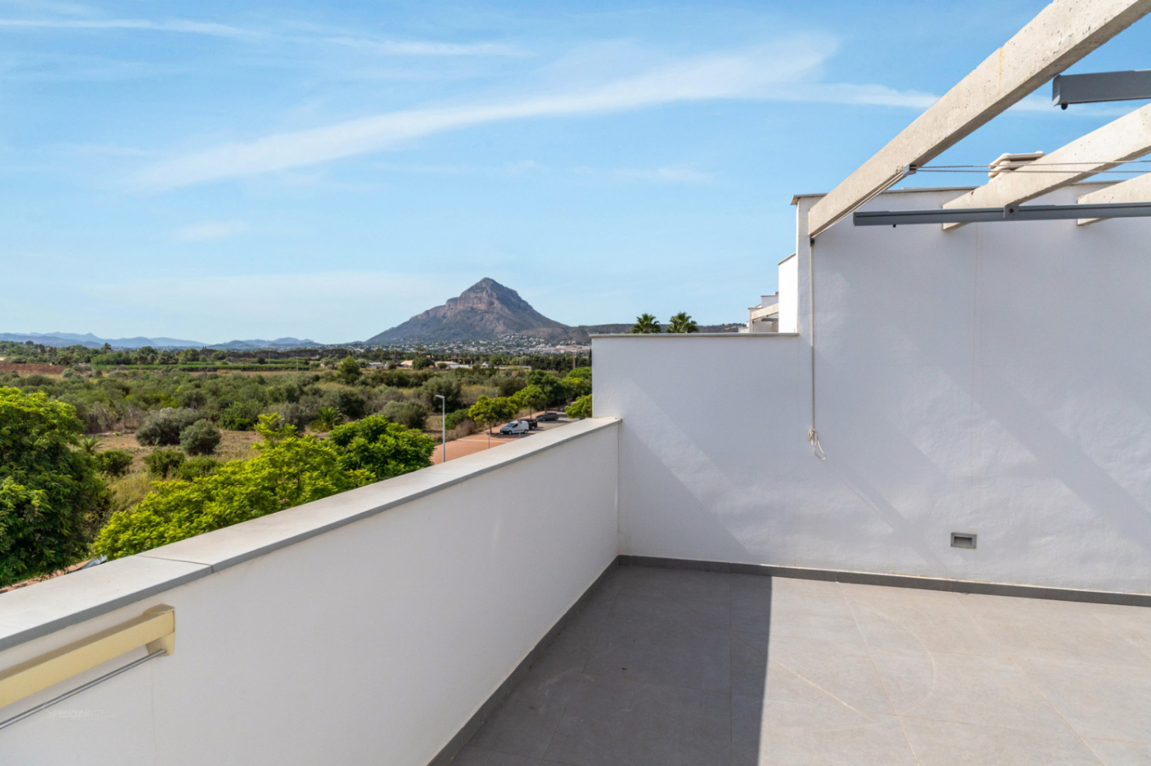 Private rooftop terrace featuring grey porcelain tiling and a concrete pergola, offering panoramic views of the Montgó mountain and protected green fields.