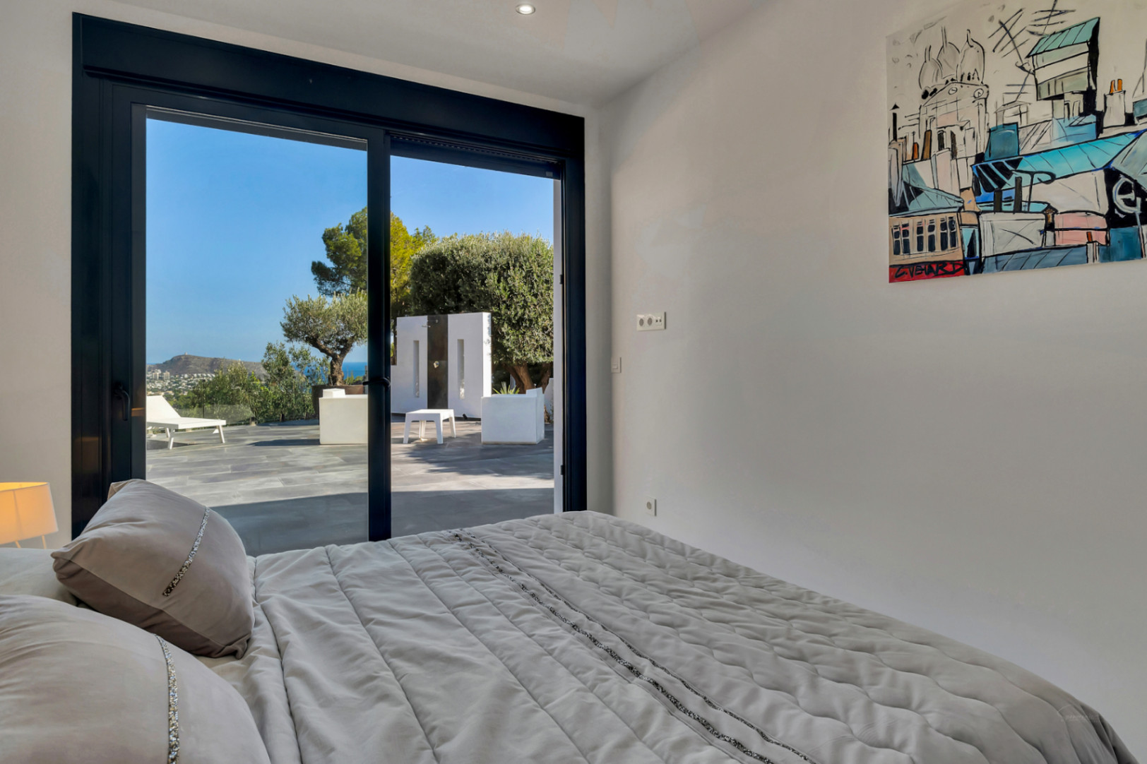 Bedroom featuring floor-to-ceiling sliding doors with direct terrace access, providing views of the Mediterranean Sea and garden from the bed.