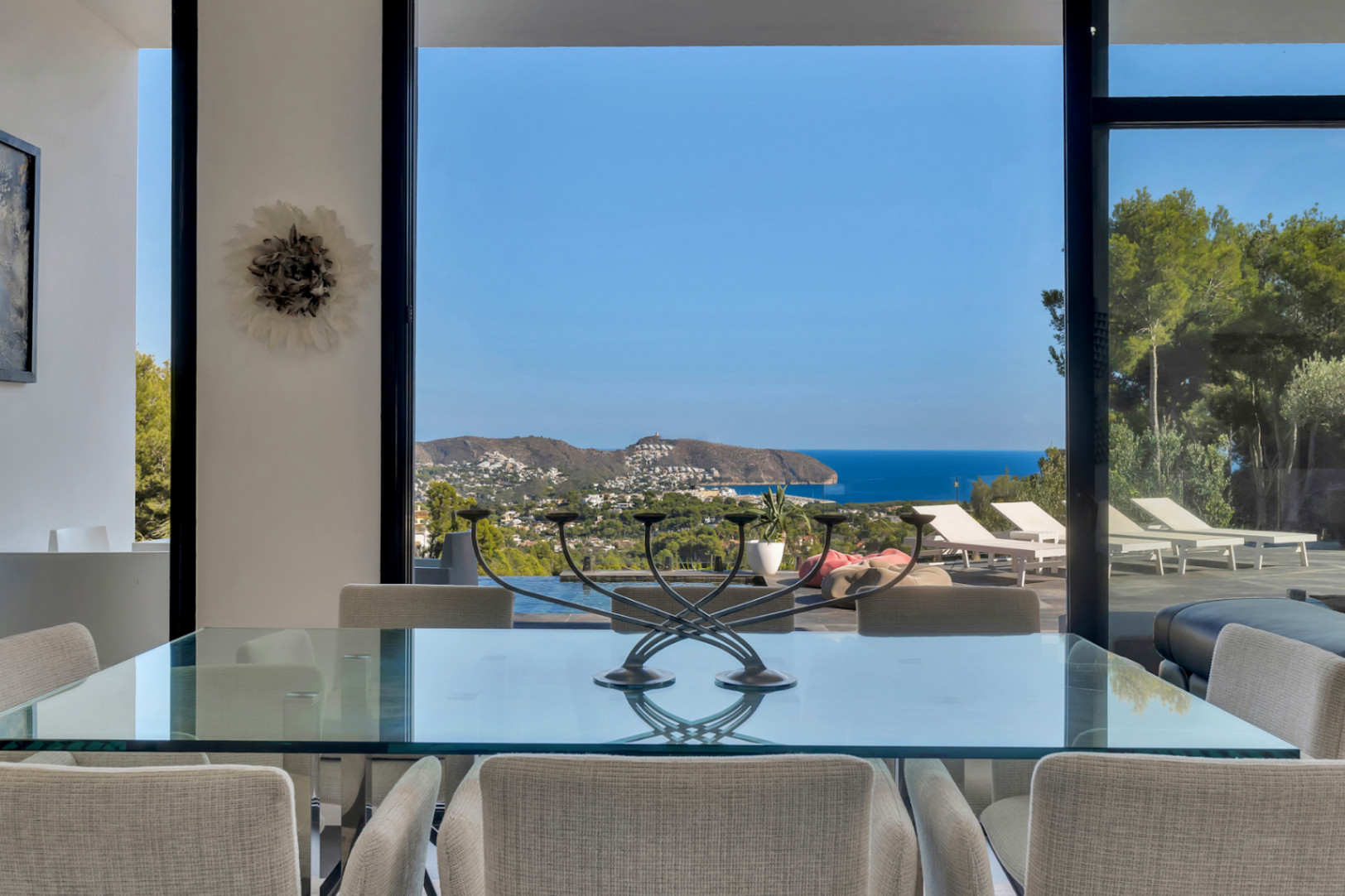 Dining area featuring a glass-top table and upholstered chairs, offering panoramic views of the Mediterranean Sea through floor-to-ceiling windows.
