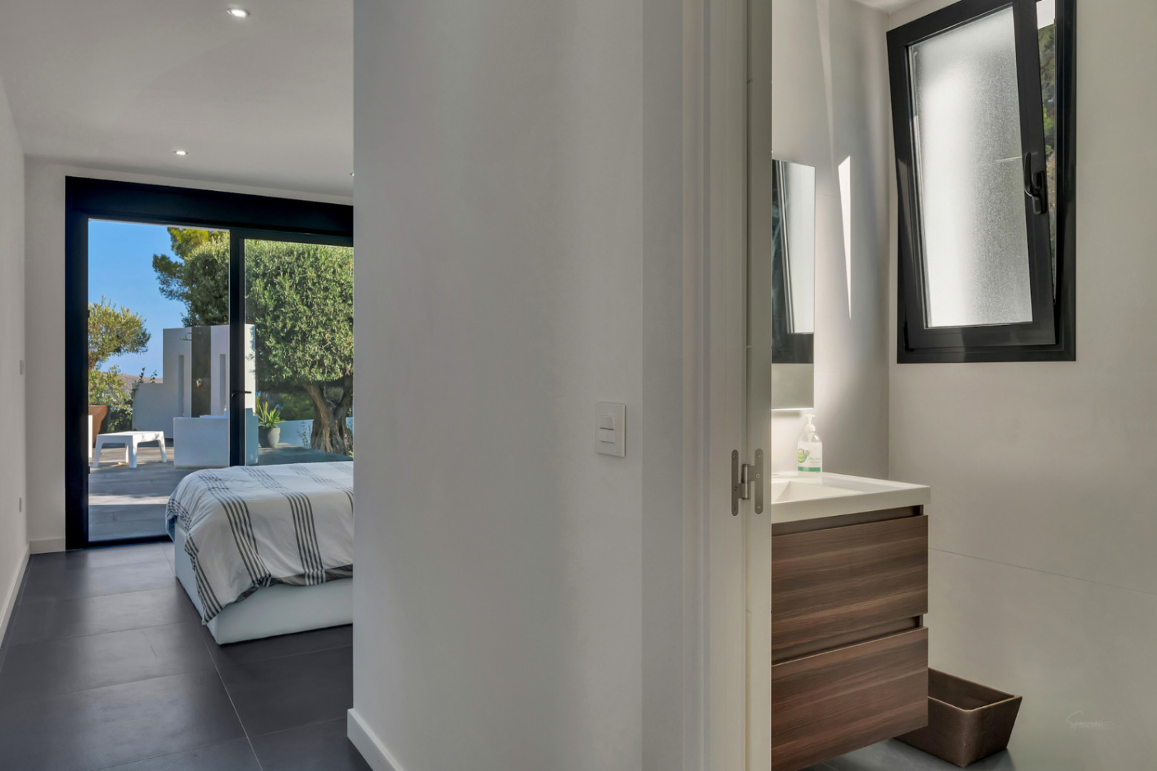 En-suite bedroom featuring dark floor tiles, direct terrace access through sliding doors, and a modern bathroom with a wood-finish vanity.