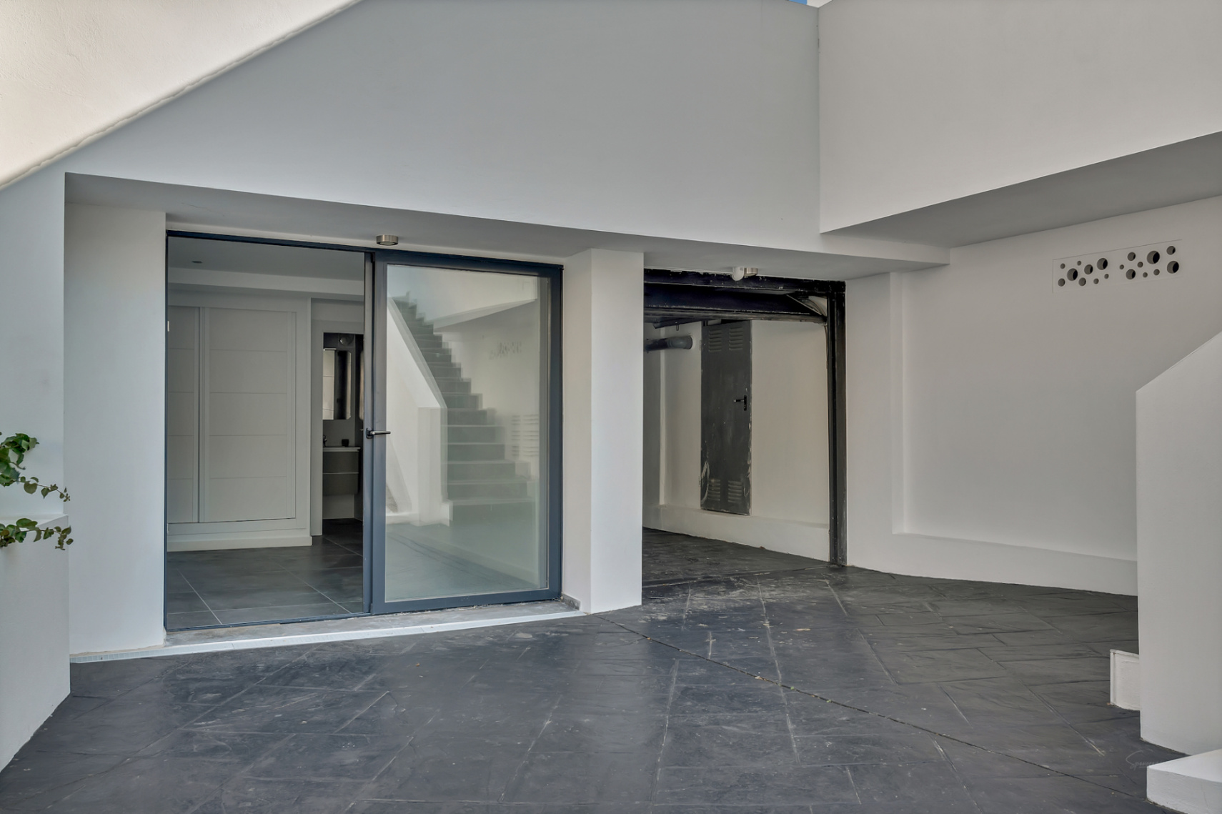 Independent lower-level entrance featuring a glass door to the guest suite and an adjacent garage area with textured dark stone paving.