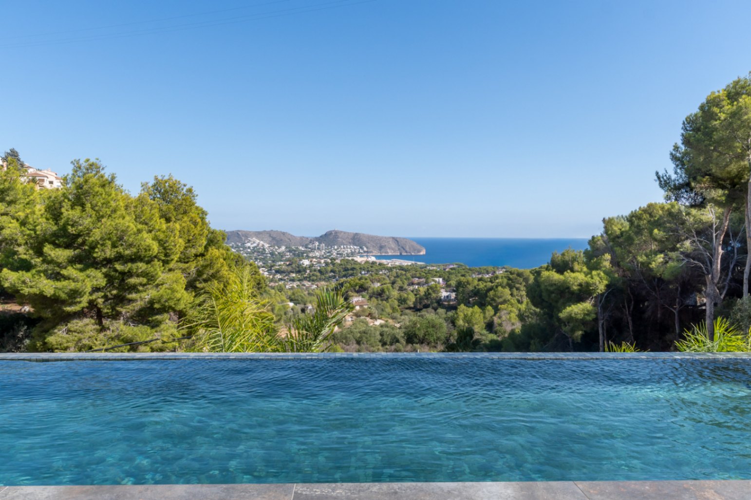 Infinity pool with blue mosaic tiling offering panoramic views of the Mediterranean Sea, the Moraira coastline, and the surrounding pine forest.