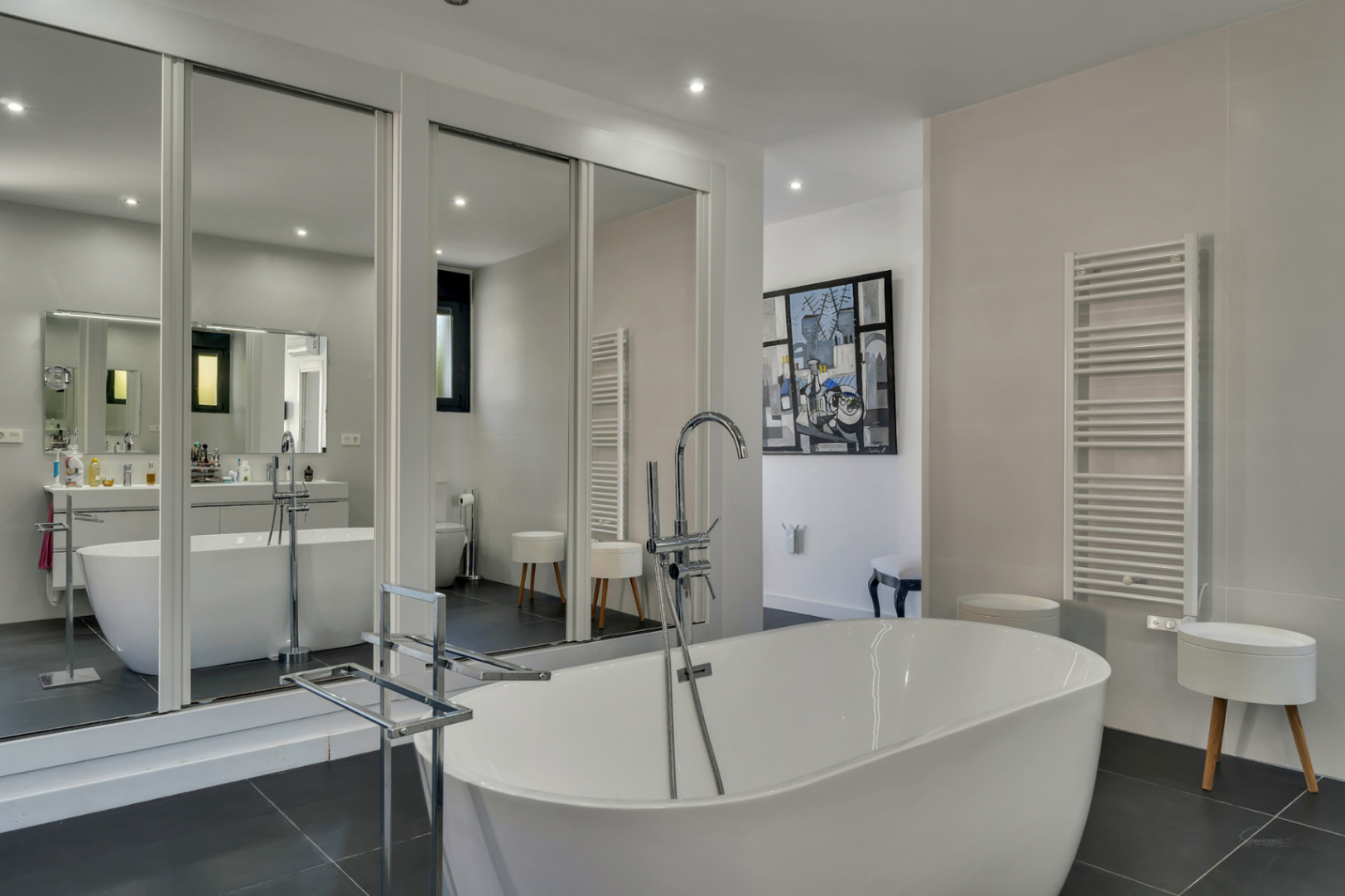 Master bathroom featuring a freestanding oval tub with floor-mounted chrome fixtures and large mirrored sliding doors reflecting the modern design.