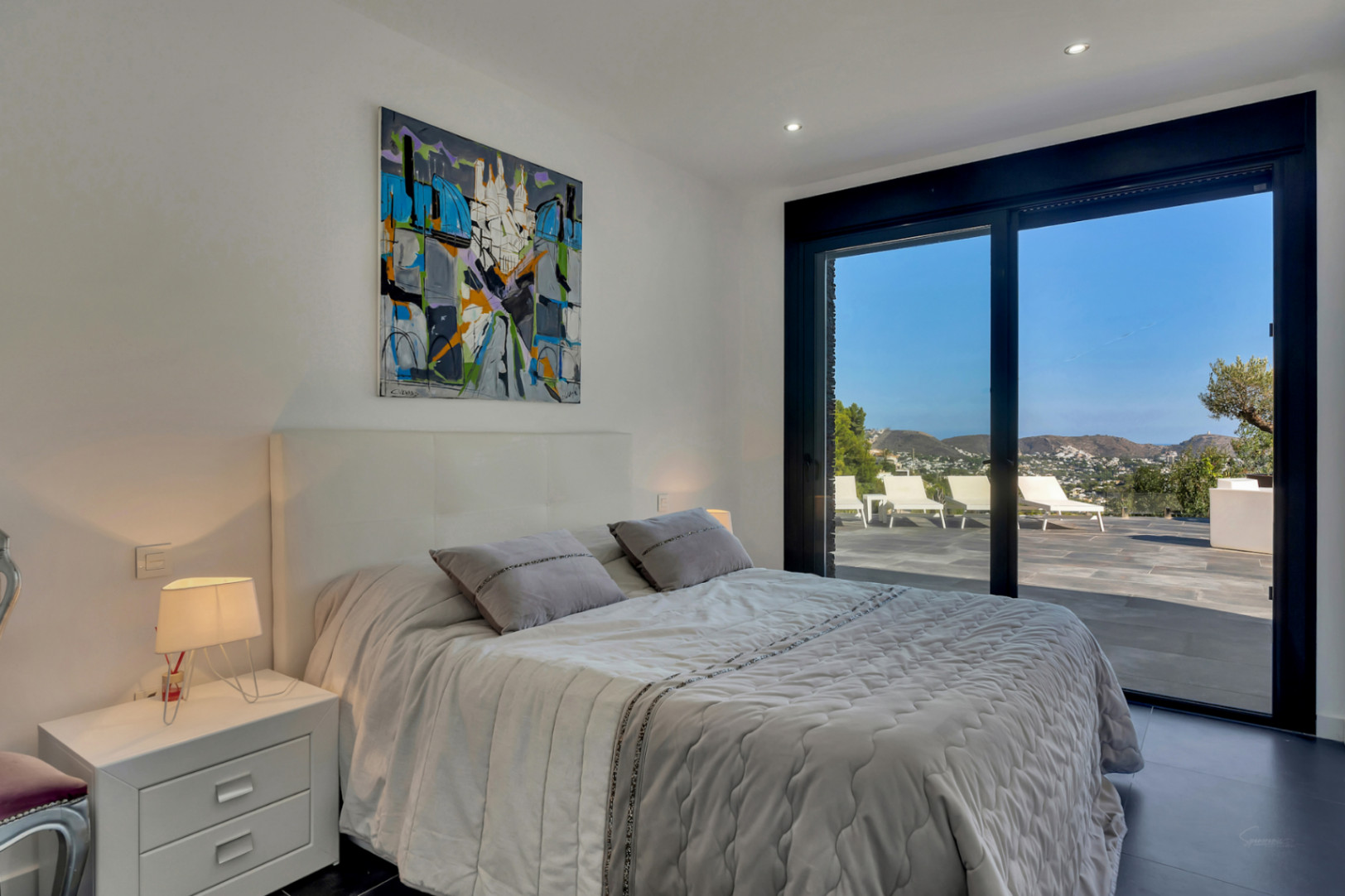 Modern bedroom featuring direct access to a private terrace. Floor-to-ceiling sliding glass doors offer panoramic mountain and sea views, complemented by minimalist design.