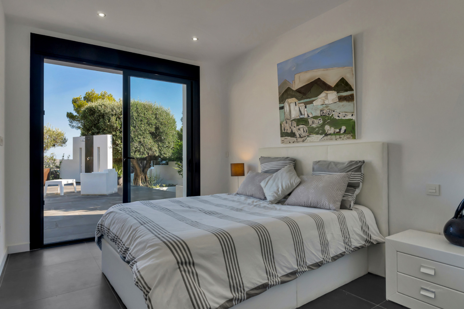 Modern bedroom with direct terrace access, black-framed sliding doors, dark ceramic flooring, and integrated recessed ceiling lighting.