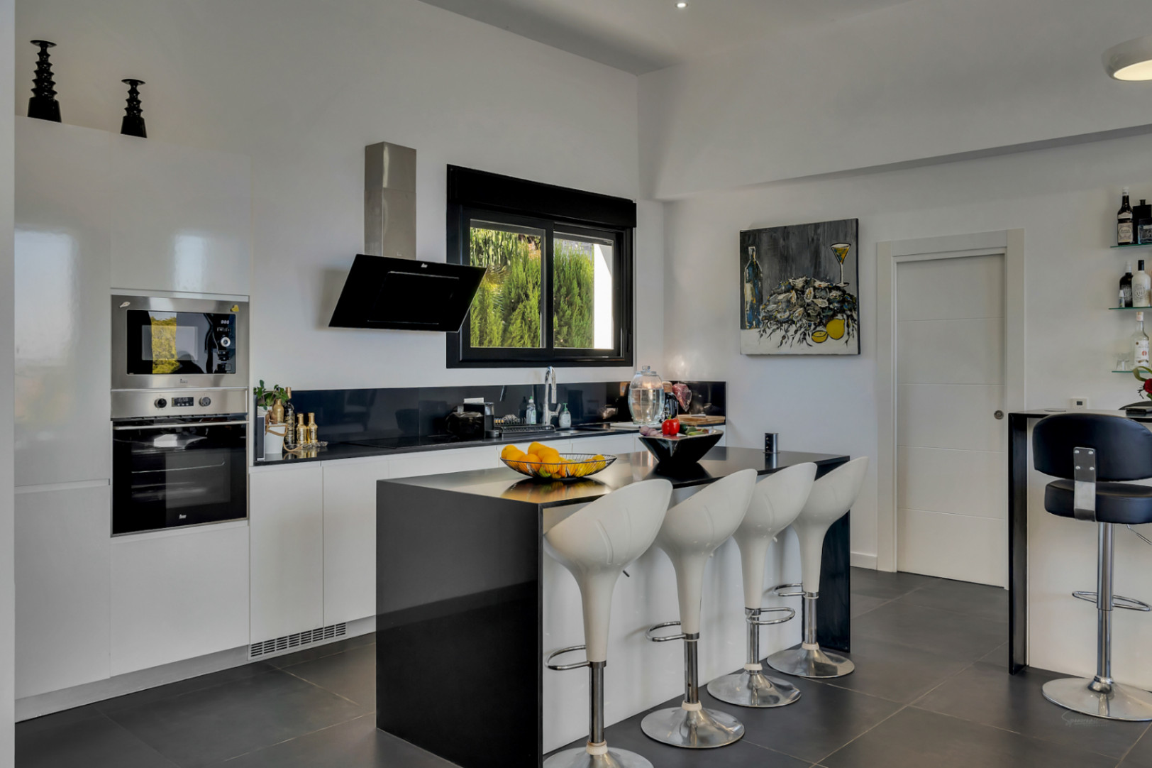 Modern kitchen featuring a black island with white bar stools, integrated stainless steel appliances, and sleek black and white cabinetry.