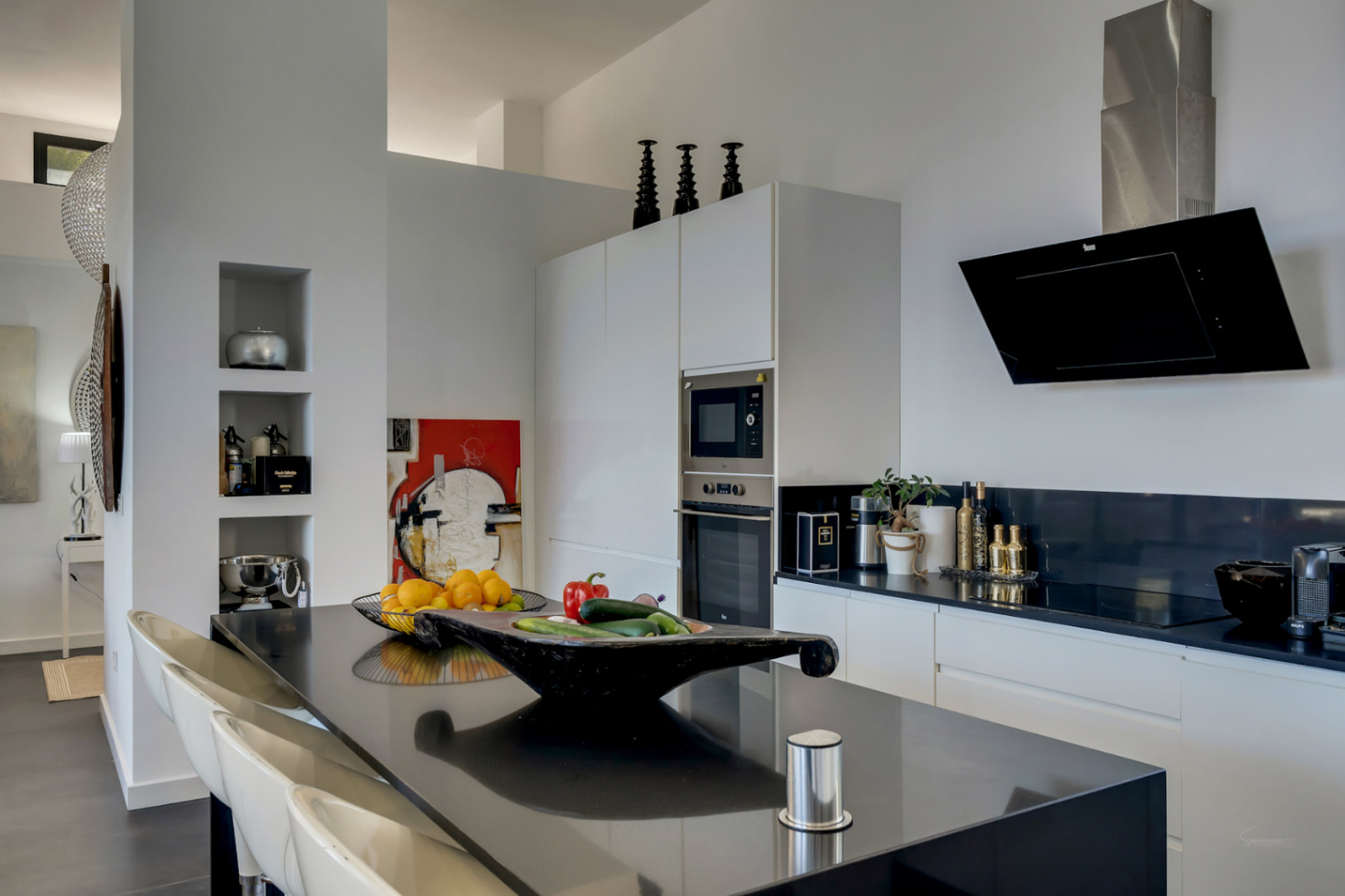 Modern kitchen featuring a sleek black island with seating, integrated appliances, and minimalist white cabinetry. Includes a designer extractor hood and built-in wall niches.