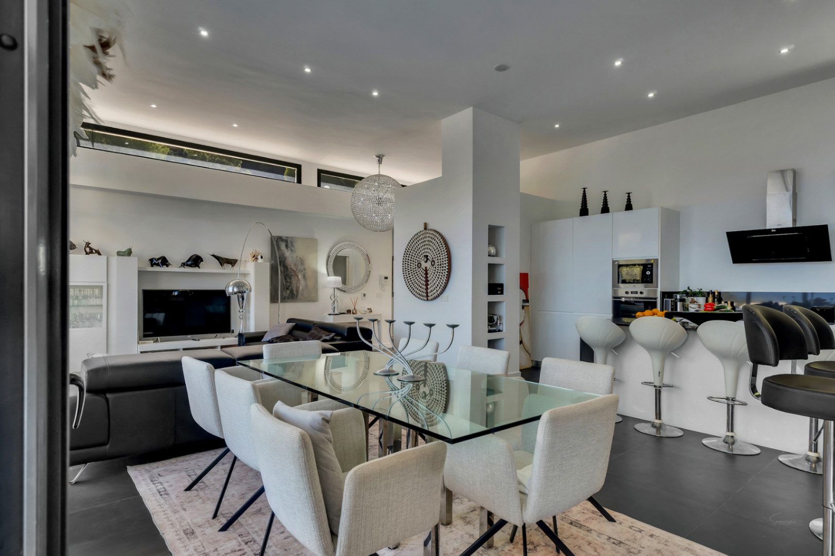 Open-concept living area featuring a glass dining table, modern kitchen with breakfast bar, high ceilings with clerestory windows, and recessed lighting.