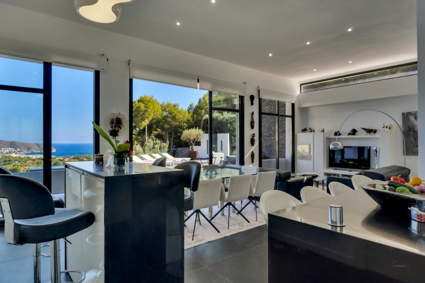Open-plan living area featuring high ceilings, floor-to-ceiling windows with sea views, and a designer kitchen with a black breakfast bar.