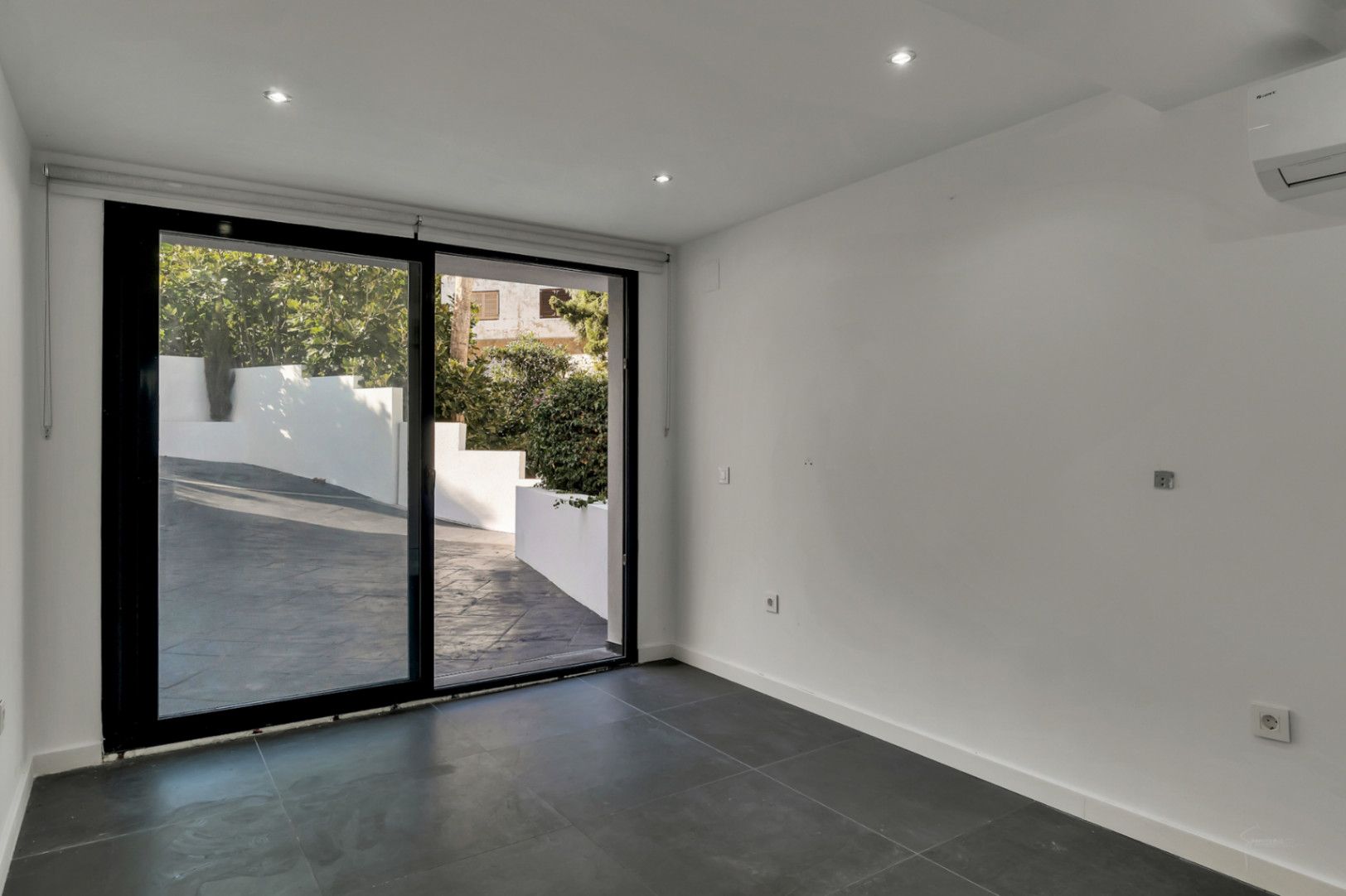 Versatile room featuring dark grey tiling, recessed LED lighting, and a large sliding glass door providing direct access to the paved exterior area.