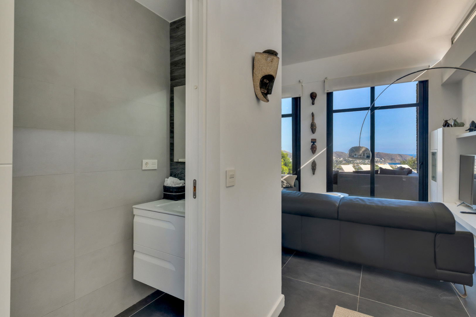 View from the guest bathroom featuring a white floating vanity, looking into the living area with floor-to-ceiling windows and coastal views.