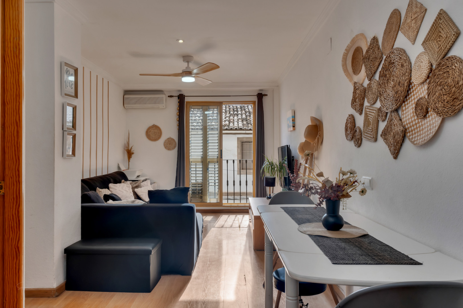 Bright living and dining area featuring wood flooring, a ceiling fan, and sliding doors opening to a balcony with views of historic tiled roofs.