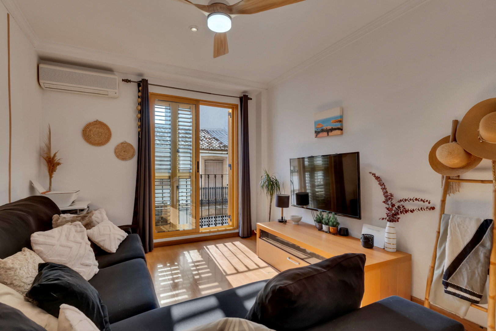 Bright living room featuring wooden flooring, air conditioning, and a balcony with traditional shutters overlooking the historic town center's architecture.