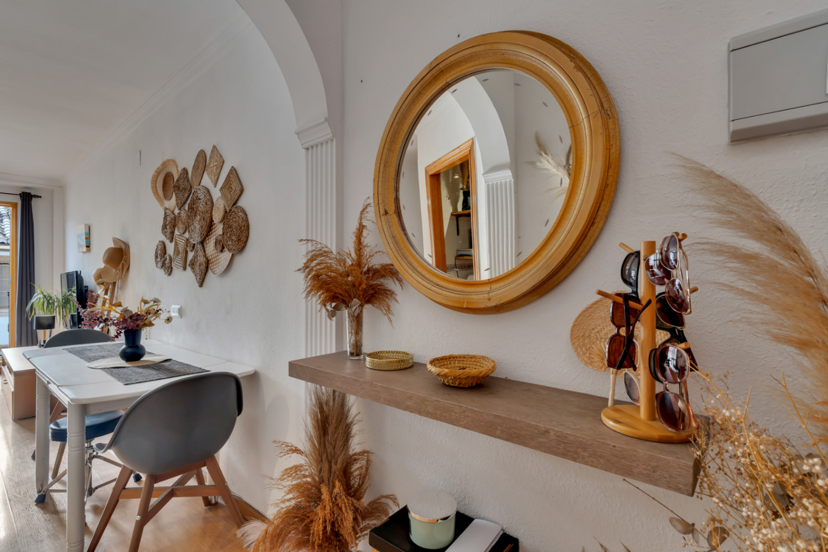 Entrance area featuring a round wooden mirror and floating shelf, seamlessly transitioning into a dining space with Mediterranean wall accents.