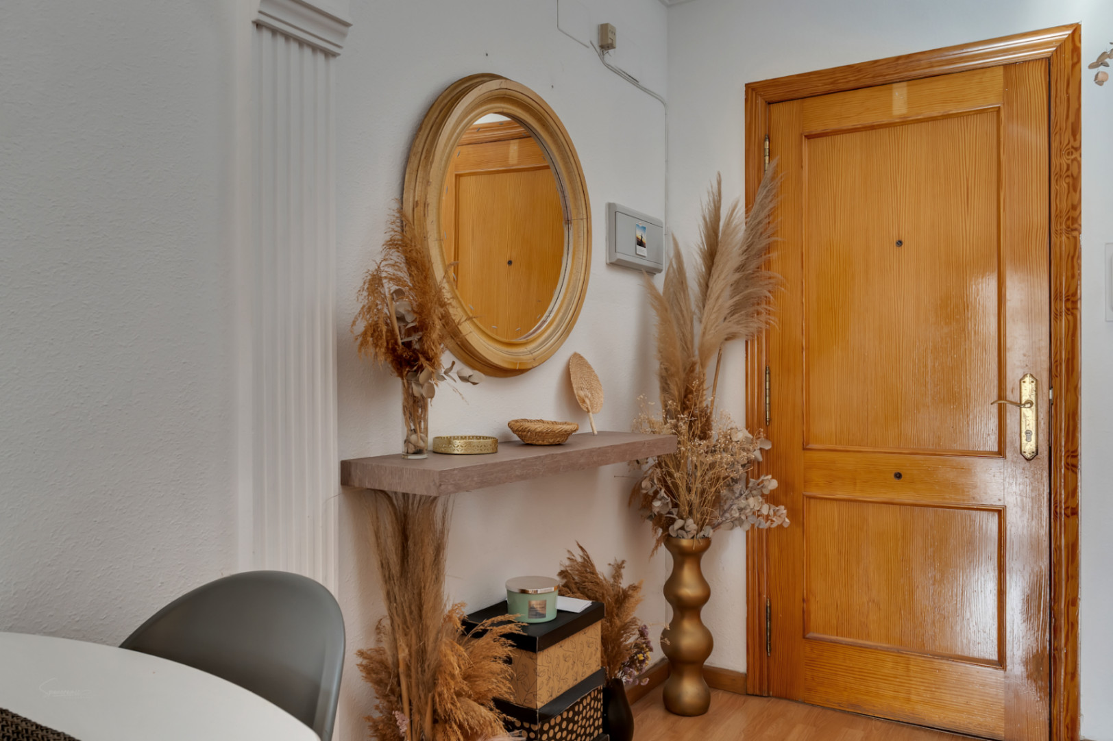 Entryway featuring a solid wood door, a circular mirror, and a floating shelf styled with dried botanical arrangements and golden accents.