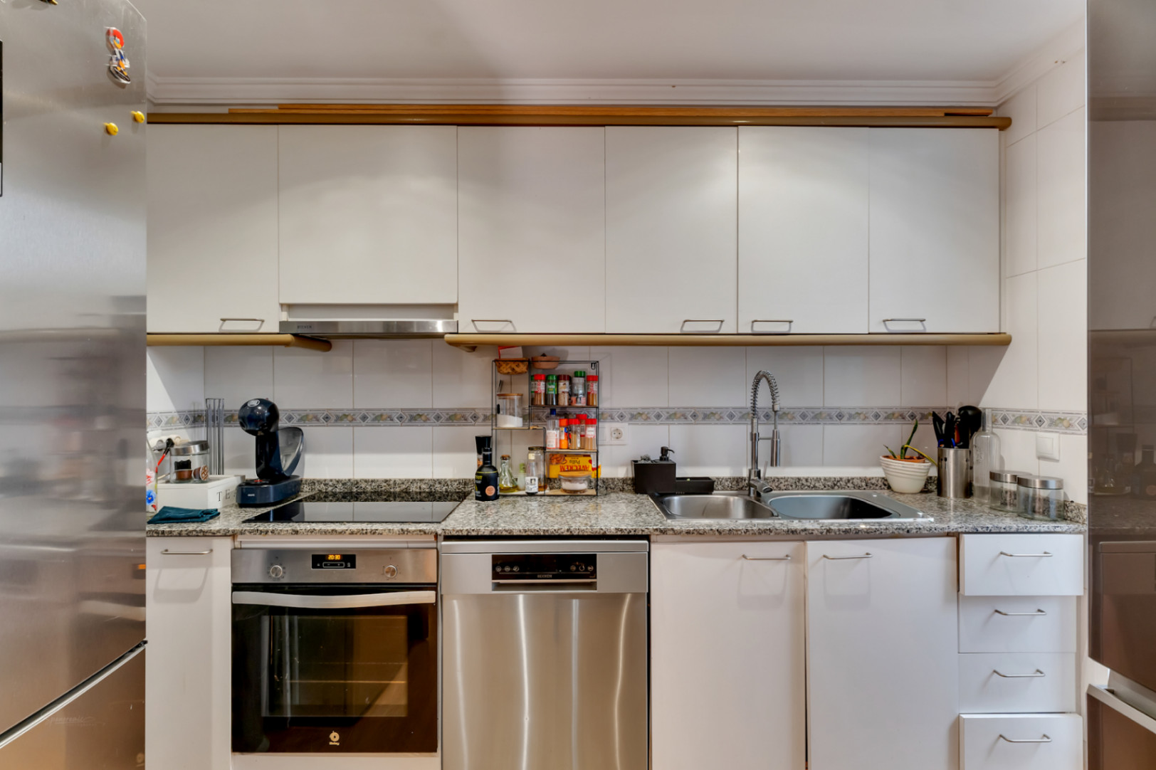 Equipped kitchen featuring white cabinetry, granite countertops, and stainless steel appliances including an integrated oven and dishwasher.