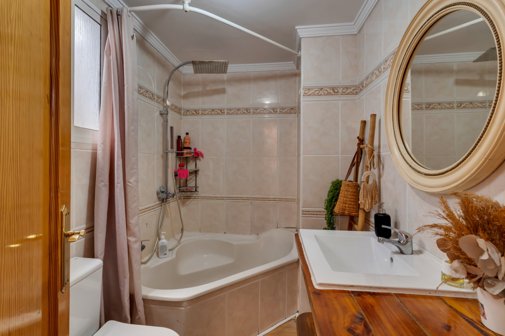 Full bathroom featuring a corner bathtub with rain shower, a rustic wooden vanity, and a circular mirror against cream-toned tiling.