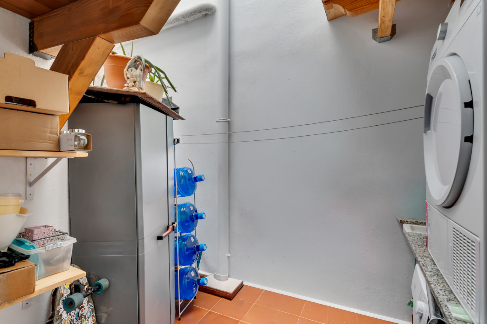 Functional interior patio featuring a laundry area, terracotta flooring, wooden beams, and organized storage solutions.