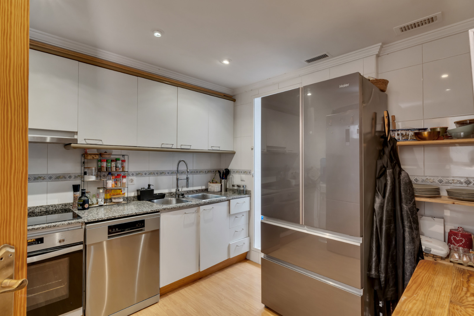 Functional kitchen featuring white cabinetry, granite countertops, and stainless steel appliances, including a large double-door refrigerator and dishwasher.