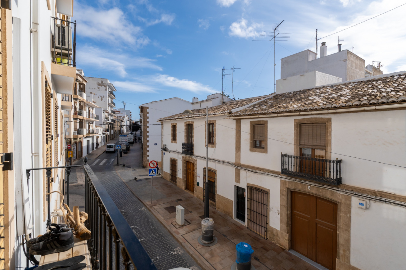 View from the balcony overlooking a street in Jávea's historic center, featuring traditional white facades with Tosca stone details and classic clay tile roofs.
