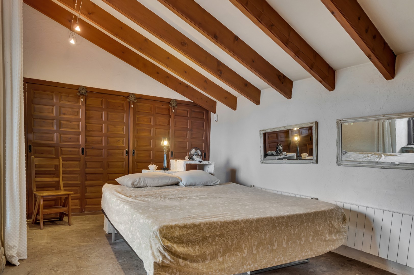 Bedroom featuring slanted ceilings with exposed wooden beams, large paneled wooden wardrobes, and textured white walls with integrated mirrors.