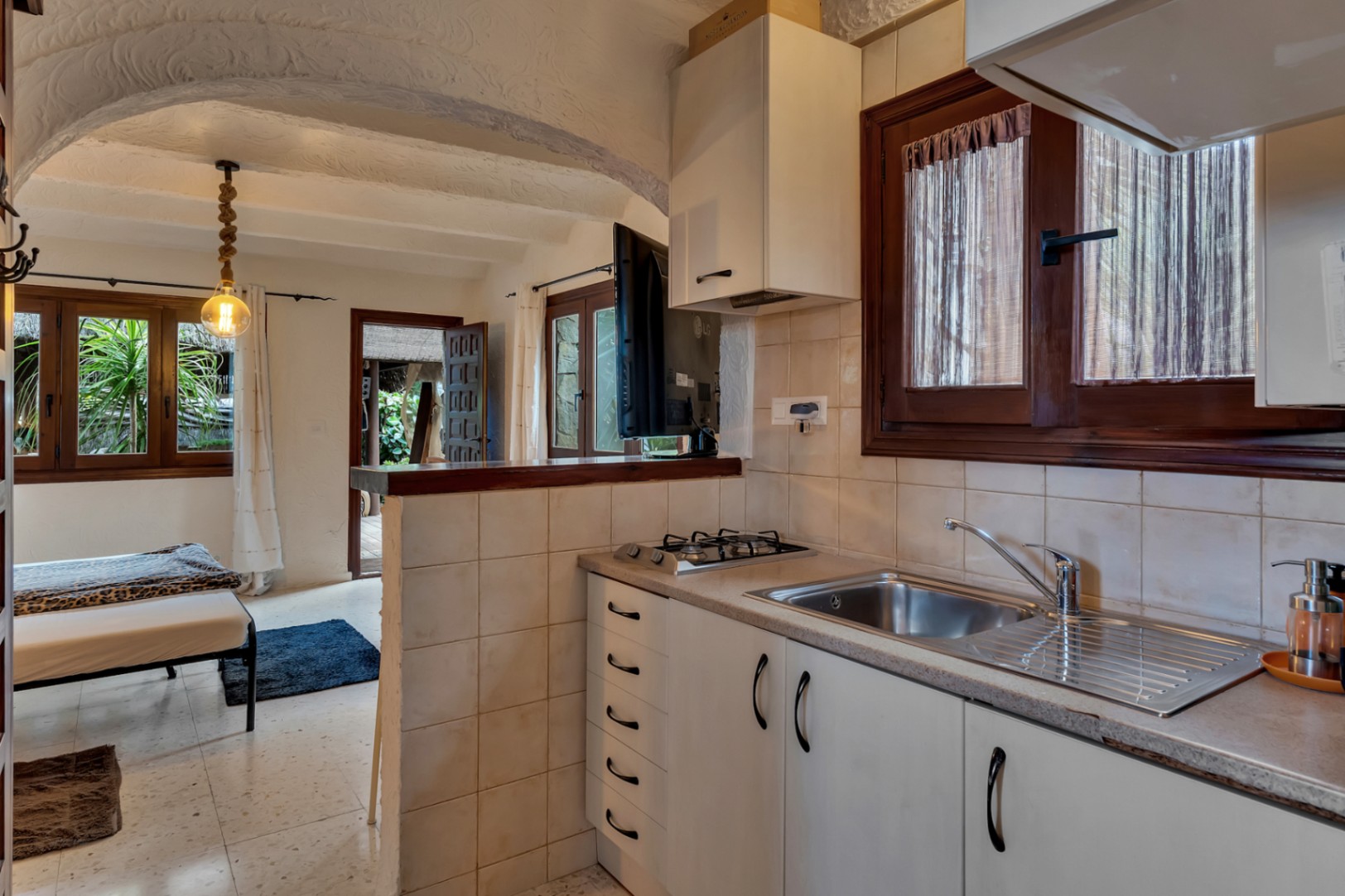 Compact guest apartment kitchen featuring white cabinetry, a gas stovetop, and a tiled half-wall under a traditional textured arched ceiling.