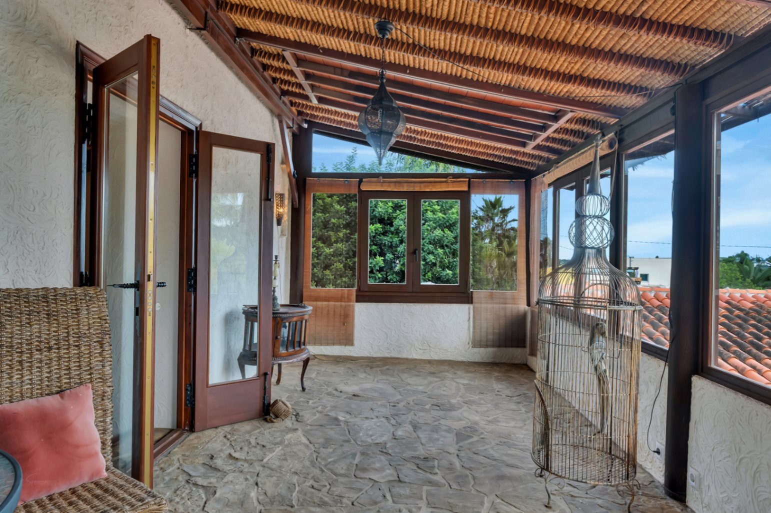 Enclosed terrace featuring natural stone flooring, a sloped wooden ceiling with reed lining, and a decorative Moroccan lantern overlooking the surroundings.