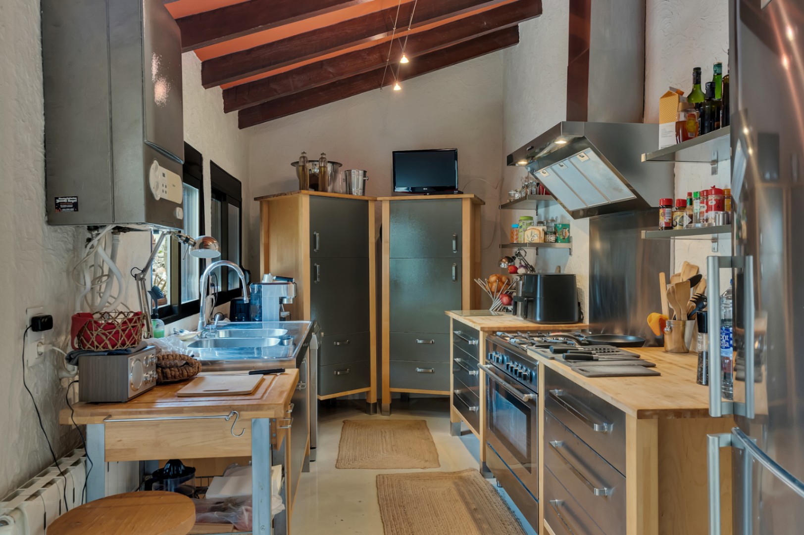 Industrial-style kitchen featuring exposed wooden beams, solid wood countertops, and stainless steel appliances under a traditional slanted ceiling.