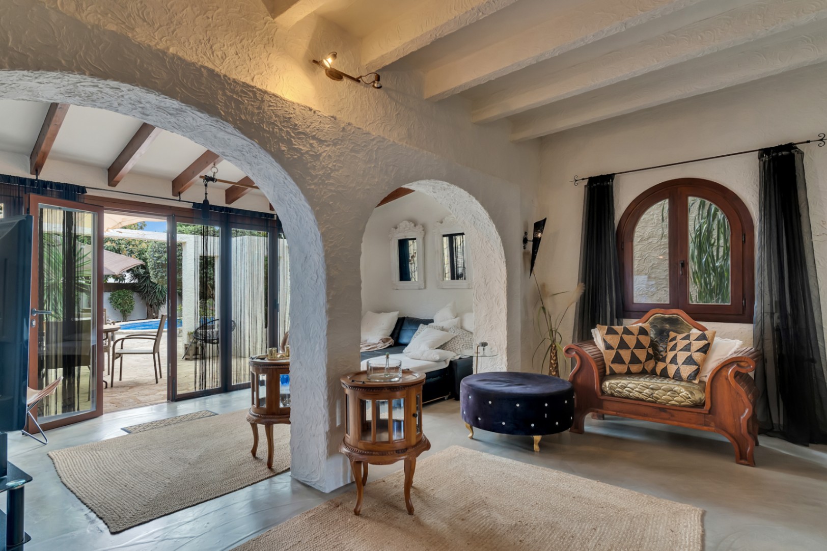 Interior living area featuring textured Mediterranean arches, exposed beams, and large glass doors connecting to the poolside terrace.