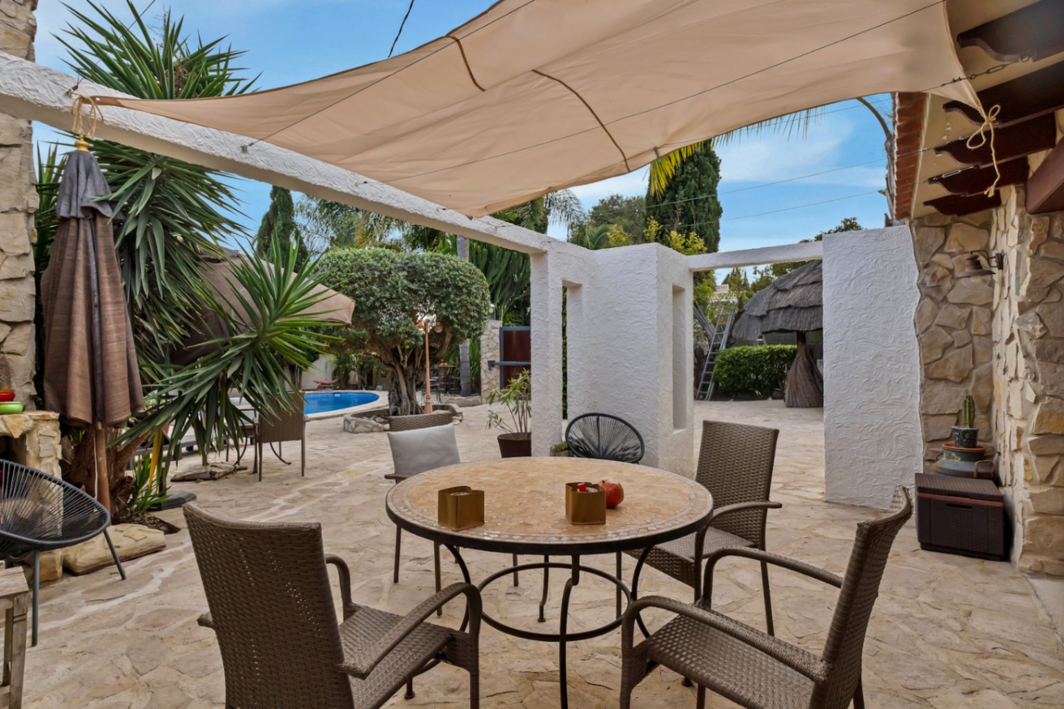 Outdoor terrace featuring natural stone flooring, a dining area shaded by a large sail awning, and views of the Mediterranean garden and pool.