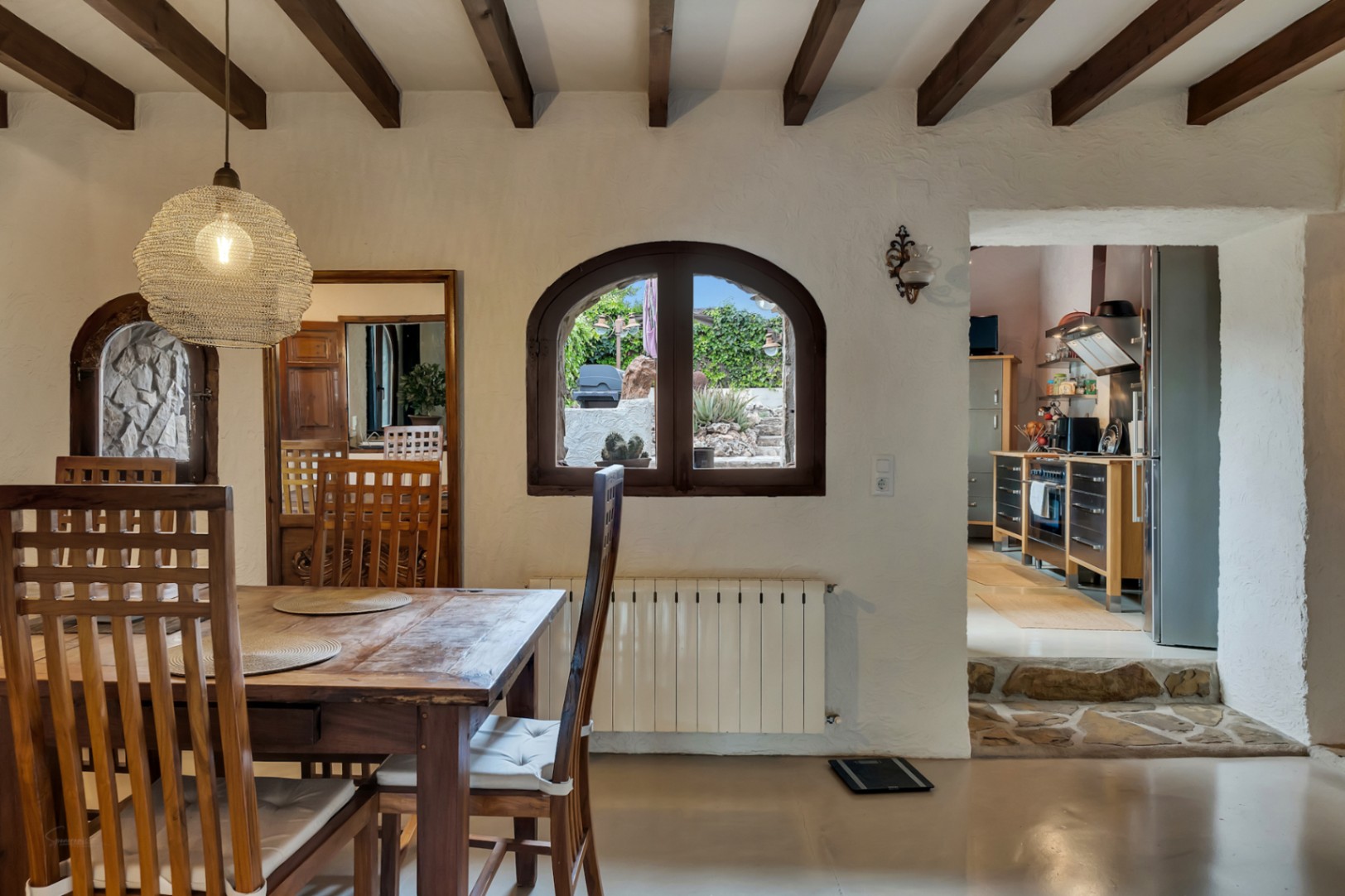 Rustic dining area featuring exposed wooden beams, a solid wood table, and stone steps leading to a modern, fully equipped kitchen.