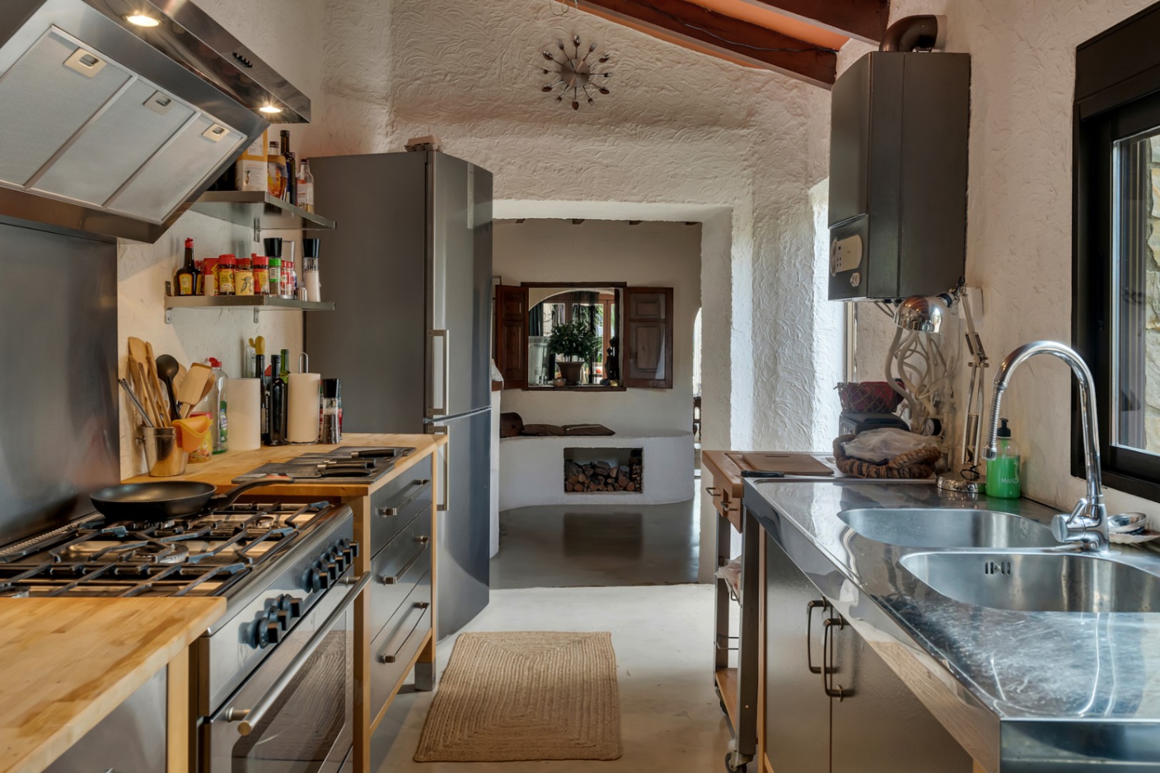Rustic-industrial kitchen featuring wood and stainless steel countertops, professional gas range, and textured walls under a beamed sloped ceiling.