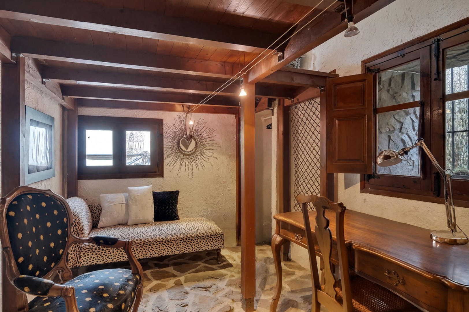 Rustic study featuring exposed wooden beams, natural stone flooring, a classic wooden desk, and an eclectic chaise longue with animal print.