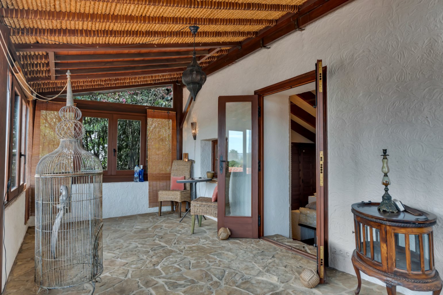 Traditional naya featuring natural stone flooring, wooden beams with reed ceiling, and wicker furniture. Large glass doors provide a seamless transition to the interior.