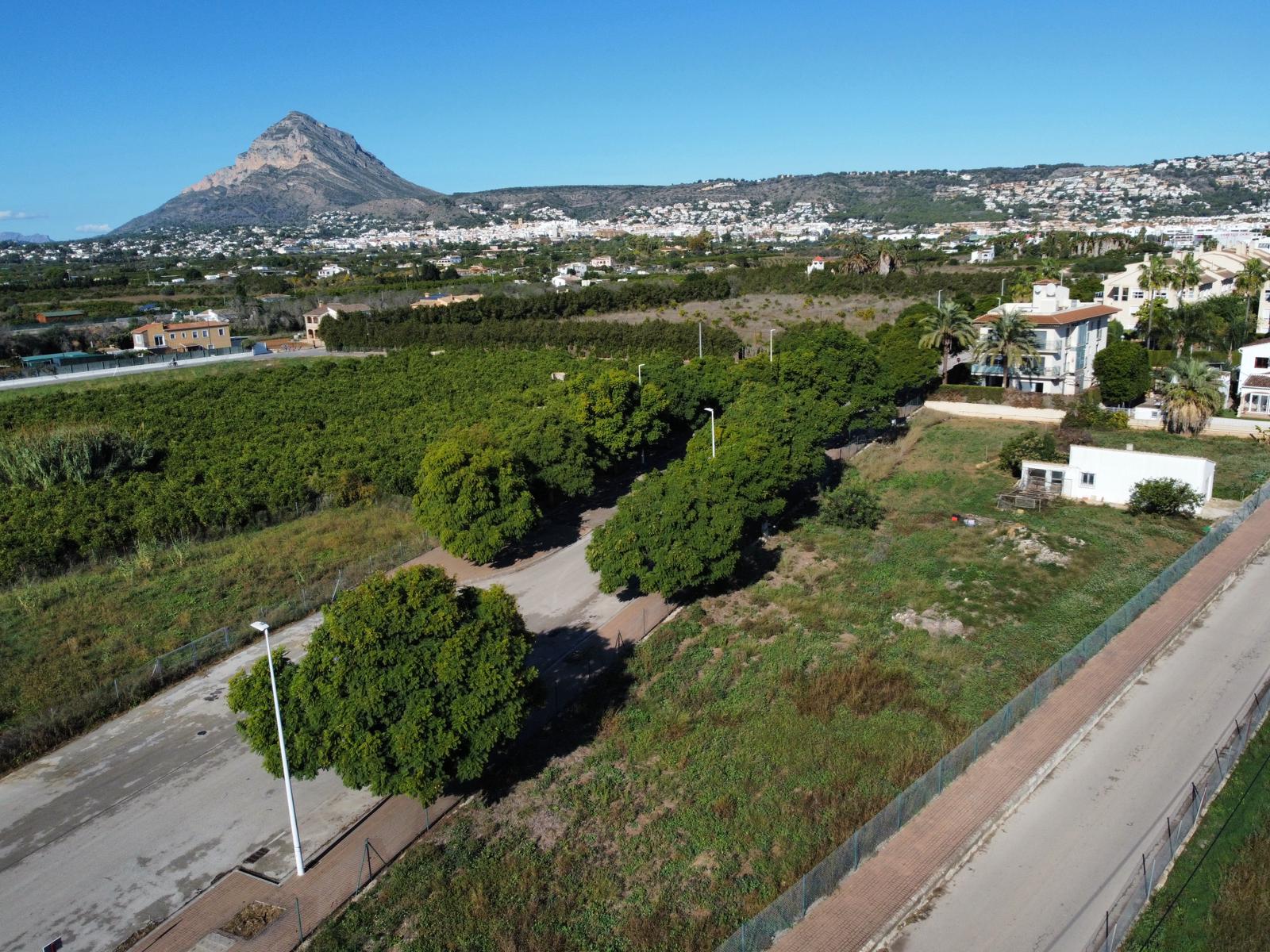 Aerial view of the residential plot in Jávea, featuring paved access roads and the iconic Montgó mountain in the background under clear skies.