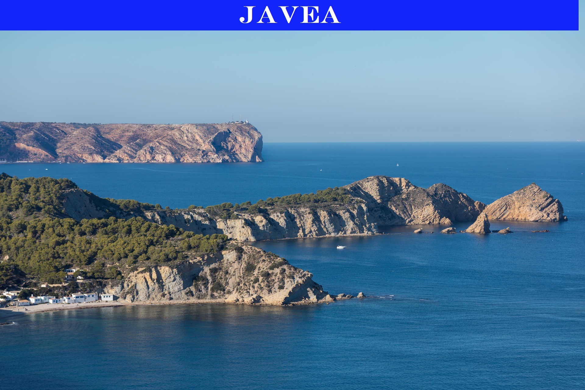 Panoramic view of the Jávea coastline featuring rugged limestone cliffs, Mediterranean pine forests, and deep blue waters under a clear sky.