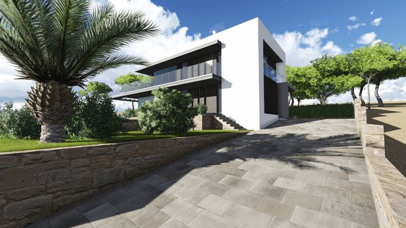 Exterior view of the modern villa showing the stone-paved driveway, natural stone walls, white facade with glass balconies, and Mediterranean landscaping.