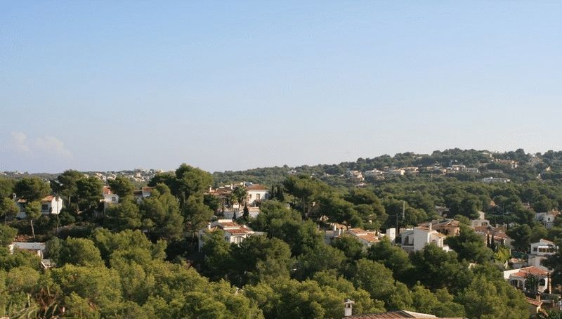 Panoramic view from the plot overlooking a residential valley with traditional white villas and dense Mediterranean pine forests.