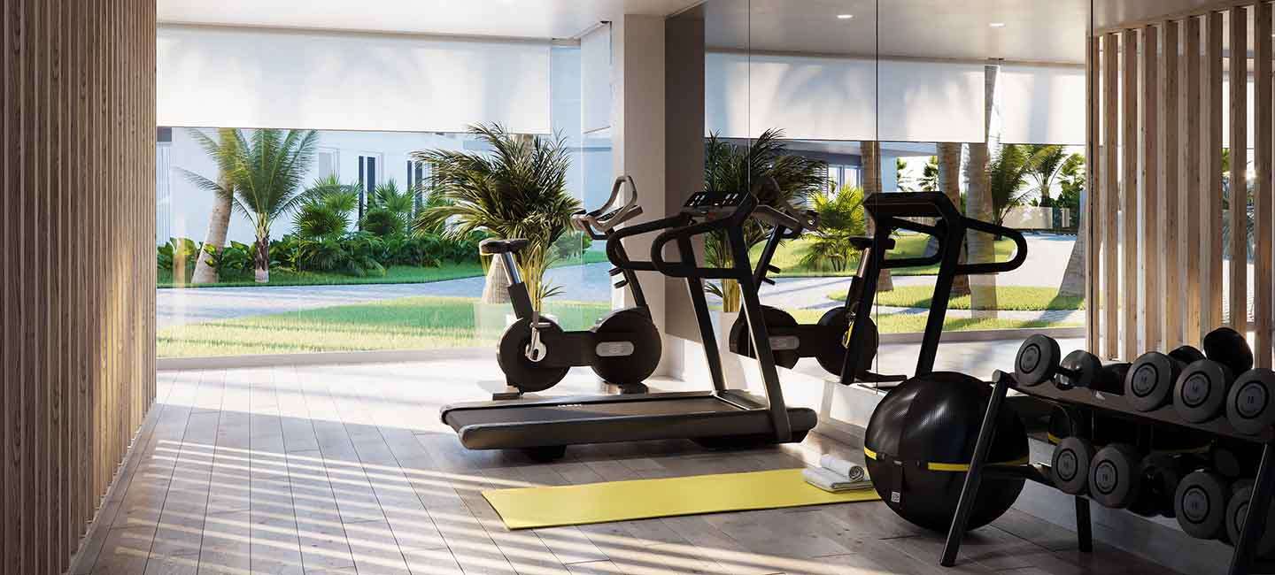Modern communal gymnasium featuring cardio equipment, free weights, and floor-to-ceiling windows overlooking lush Mediterranean gardens.