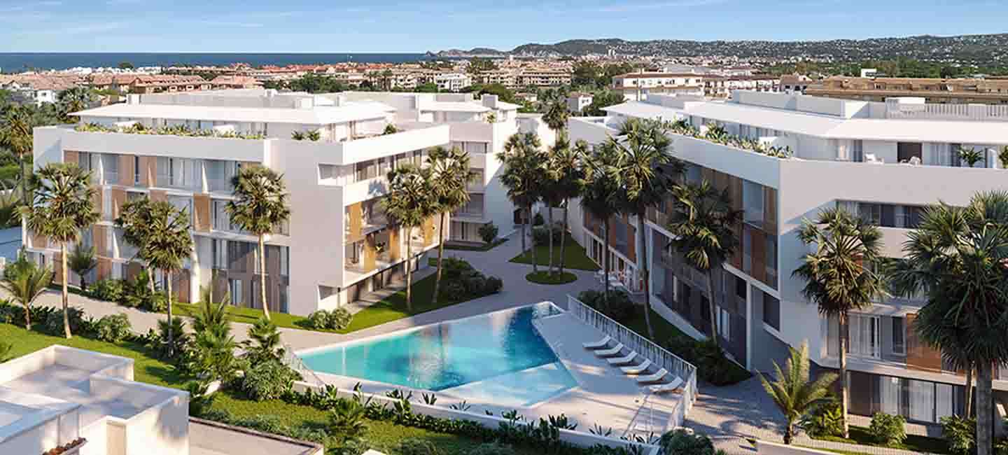 Aerial view of the contemporary apartment complex showing white buildings with wooden shutters, a triangular swimming pool, and landscaped gardens with palm trees.