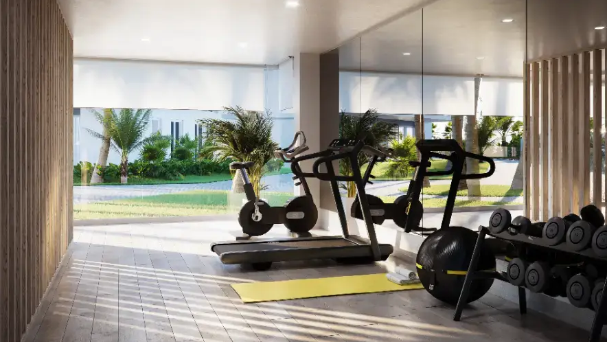 Modern gymnasium featuring cardio equipment, free weights, and floor-to-ceiling windows overlooking lush Mediterranean gardens. The space includes wood-slat wall paneling.