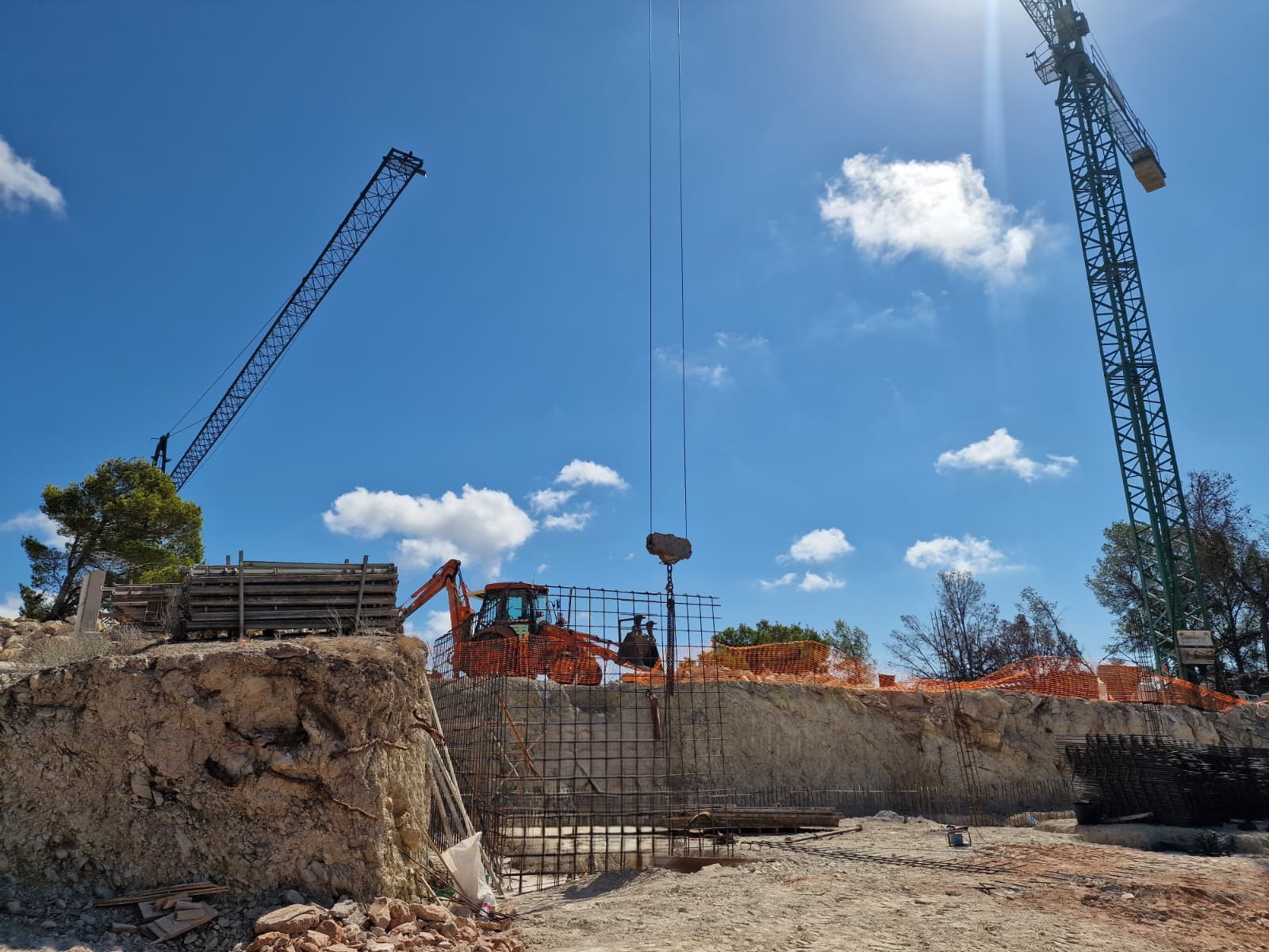 Construction progress in Moraira featuring site excavation, steel reinforcement mesh for foundations, and heavy machinery including tower cranes.